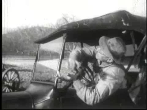 Driver in vintage car operating steering wheel with frantic expression.
