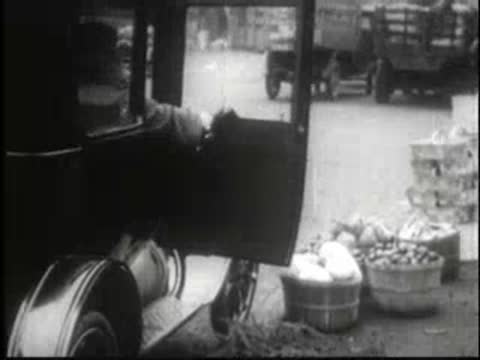 Woman getting into vintage car parked near fruit crates in town.