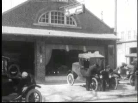 Antique cars parked in front of a large barn with arched window.