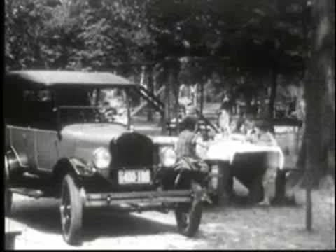 Vintage car parked near a picnic table with people sitting around it.