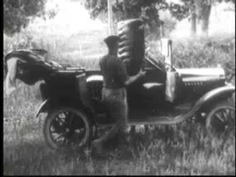 Person loading a tire into the back of a vintage convertible car.