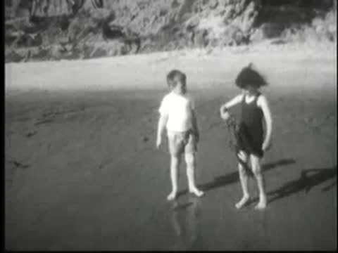 Two children play on a beach, finding a small sea creature.