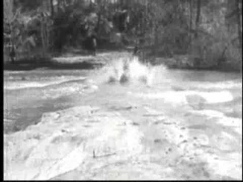 Foaming water and a vintage car driving through a shallow ford.
