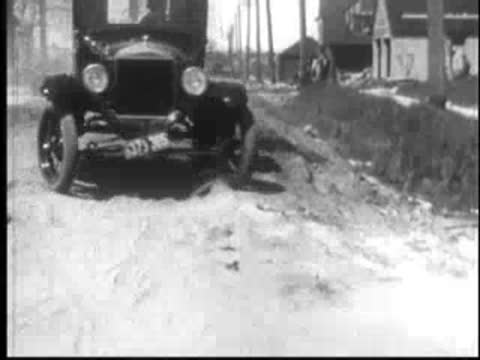 Vintage car driving on a dirt road through a rural landscape.