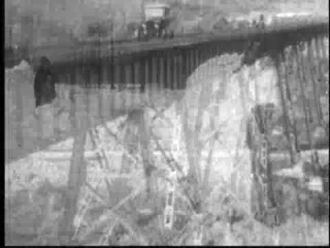 Vintage car driving through snow-covered landscape and across a high bridge.