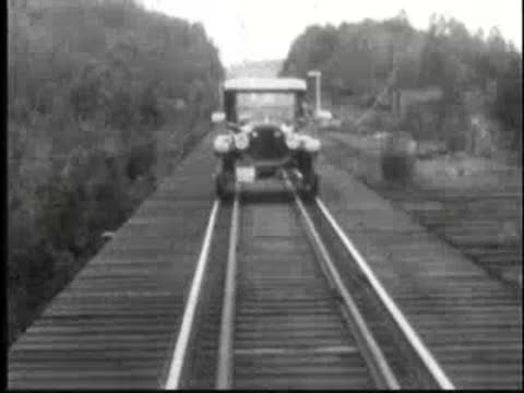Vintage car driving forward along elevated railroad tracks.