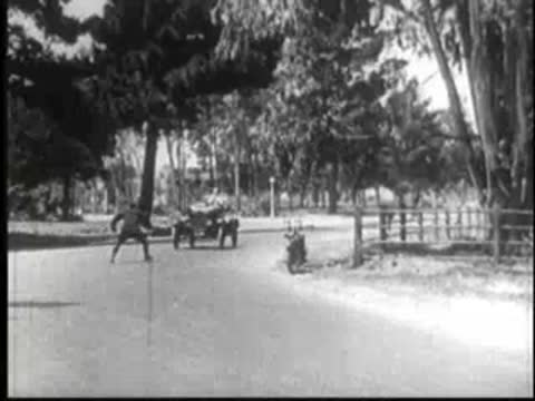 Police officer on a motorcycle pursuing a vintage car around a bend.