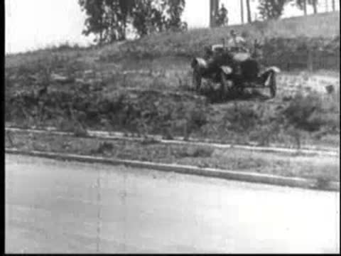 Vintage car driving down a grassy embankment onto a paved road.