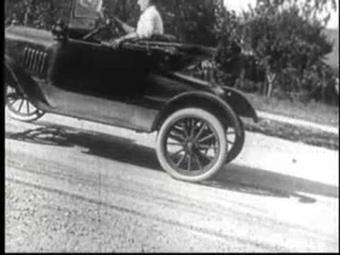 Vintage car driving on a road, tilting on two wheels during a sharp turn.