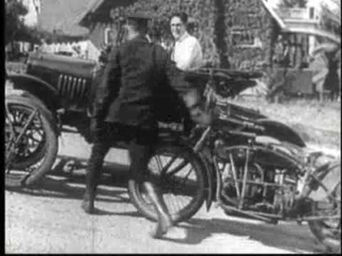 Vintage car stopped on a road, surrounded by police officers and motorcycles.