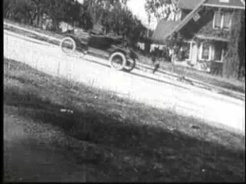 Vintage car driving quickly down a steep residential street.
