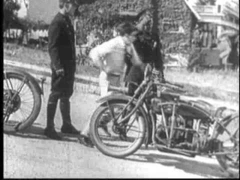 Man talking to police officers next to a parked motorcycle.