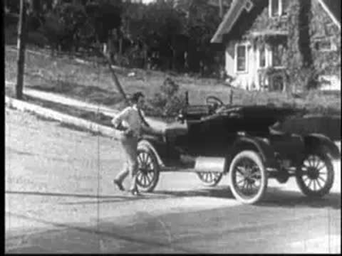 Vintage car rolling down a suburban street with a long pole attached.