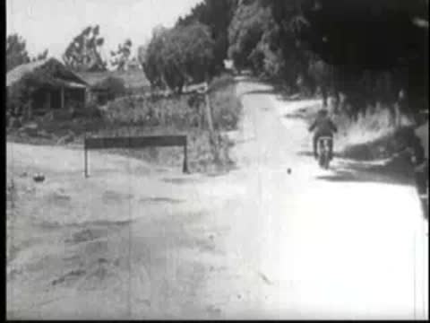 Motorcycle driving past a broken barrier gate toward an industrial factory.