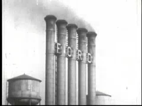 Smokestacks with FORD lettering against a bright sky, factory buildings below.