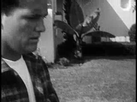 Driver opening liquor bottle outdoors near house, vintage setting, 1960s