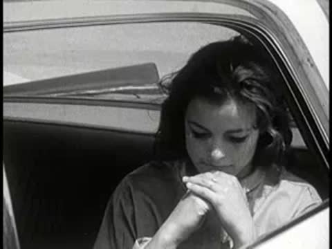 Woman sitting in passenger seat of car looking distressed, vintage setting, 1960s