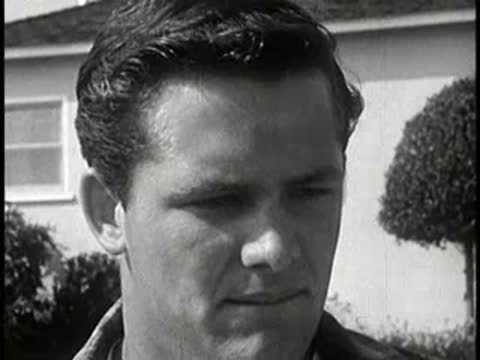 Driver looking down and talking outdoors near house, vintage setting, 1960s