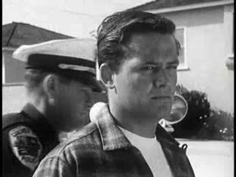 Driver looking sideways near vintage car, police officer in background, 1960s