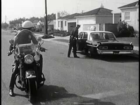 Police officer getting into patrol car on suburban street, 1960s