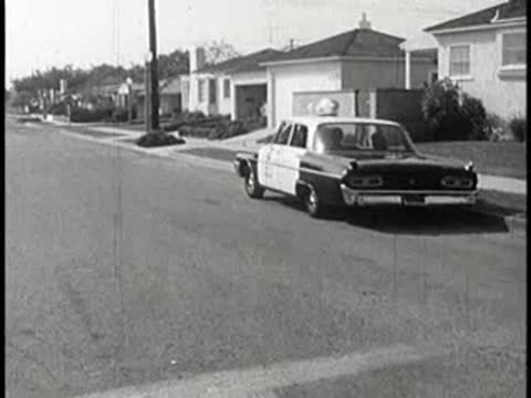 Police car driving away on suburban street, 1960s