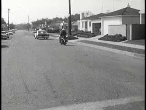 Police car and motorcycle driving down suburban street, 1960s