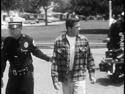 Police officer escorting a young man on the street.