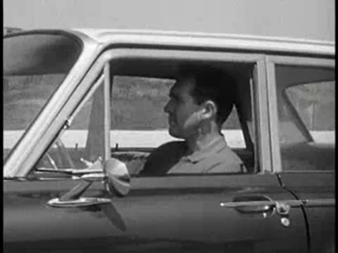 Driver inside a vintage car looking ahead on a road, vintage educational film.