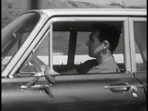 Driver profile view inside a car driving on a road, vintage educational film.