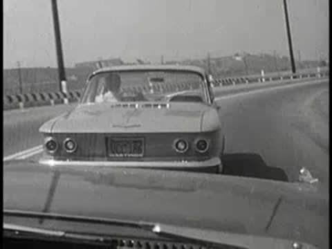 View of a car driving on a road from behind, vintage educational film.
