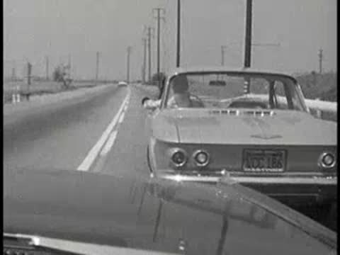 A car driving ahead on a road with another car following, vintage educational film.