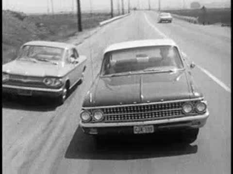 Cars driving on a multi-lane road from a rear perspective, vintage educational film.