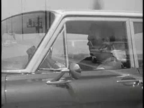 Driver rubbing his head while sitting inside a parked car, vintage educational film.