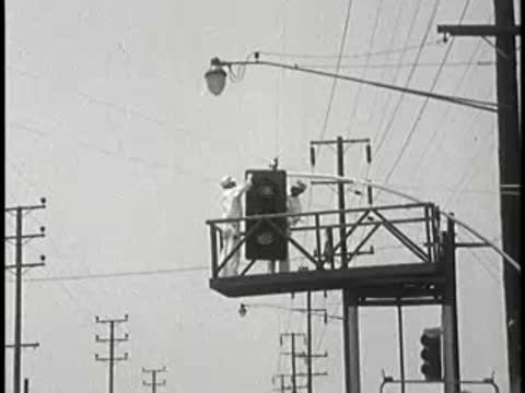 Two workers on an elevated platform near power lines, vintage educational film.