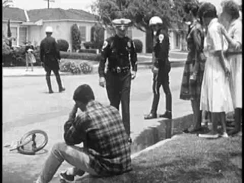 Police officers and bystanders standing around a street scene.