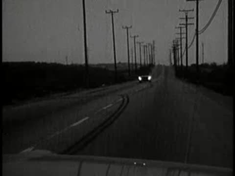 night driving view from car approaching another vehicle on road, 1960s