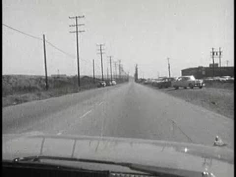 daytime driving view approaching parked cars along roadside, 1960s