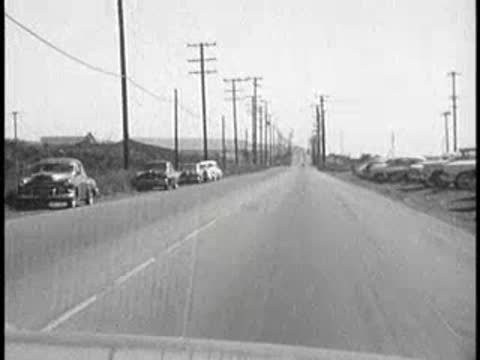 daytime driving view passing parked cars on roadside, 1960s