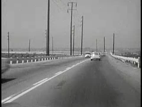 daytime driving view approaching bridge on curved road, 1960s