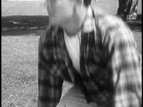 Young man in plaid shirt gets up from the grass.