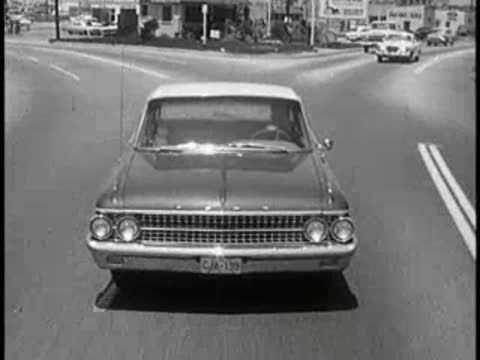 daytime view of vintage car approaching intersection, 1960s