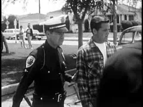 Police officer leading a young man away near an ambulance.