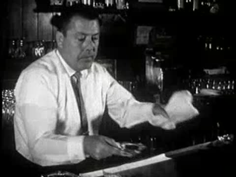 Bartender wiping counter in a tavern, 1960s interior details.