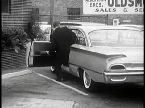Man getting into a parked two-door sedan near car sales.