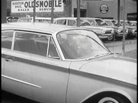 Front view of a white car parked on a street near car sales.