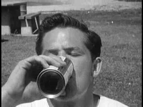 Young man drinking from a can outdoors in a park.