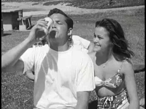 Young man drinking from a can while sitting outdoors with a woman.