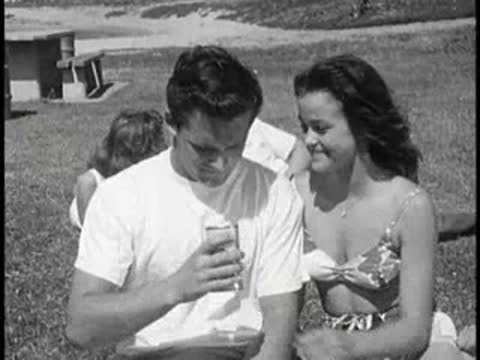 Young couple sitting together on grass, one man drinking.