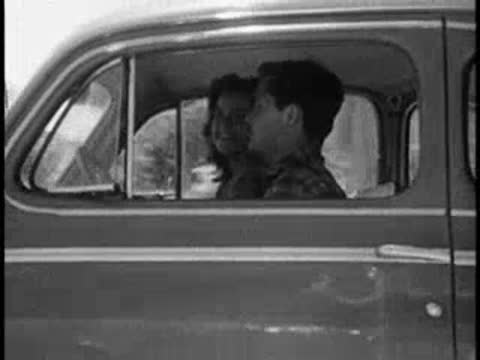 Side profile of a man and woman driving inside a vintage car.