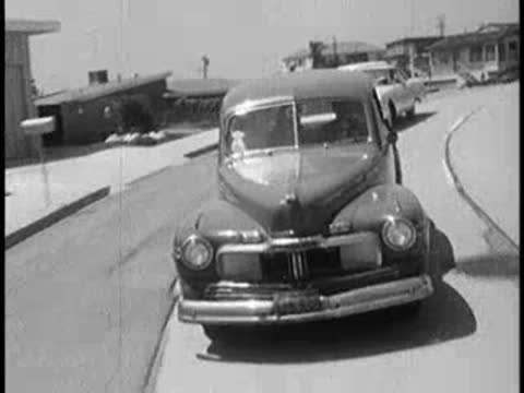 Vintage car driving forward along a curved suburban street.